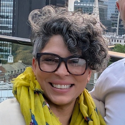 Shamain Webster, smiling, in glasses and a yellow scarf